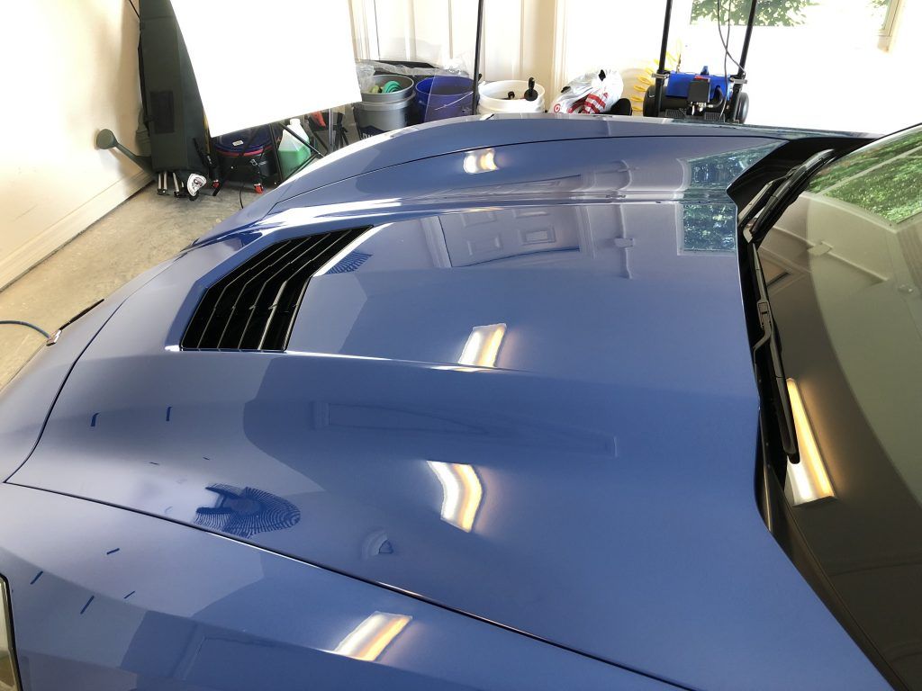 The hood of a blue sports car is sitting in a garage.