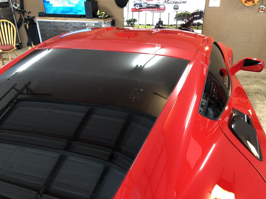 A red sports car with a black roof is parked in a garage.