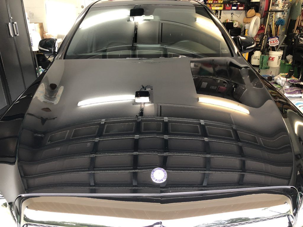A black car is parked in a garage with the hood up.