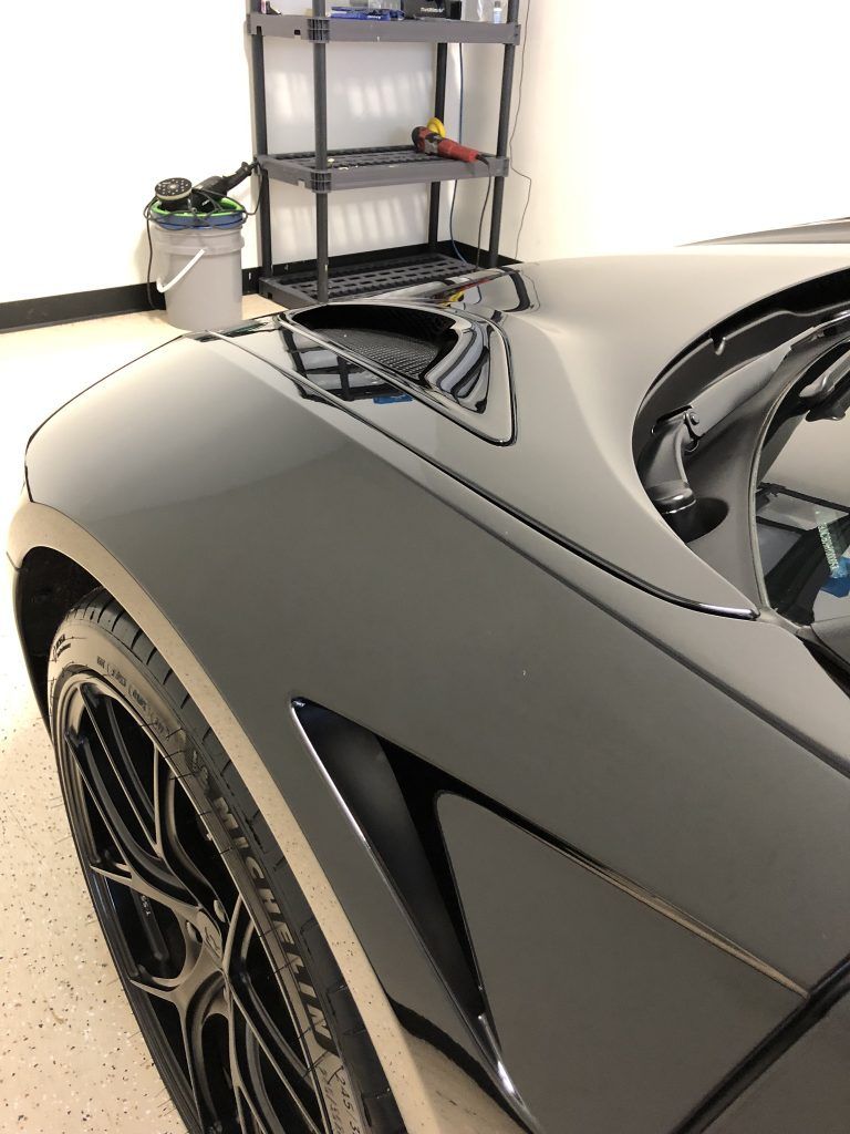 A black sports car is parked in a garage next to a shelf.