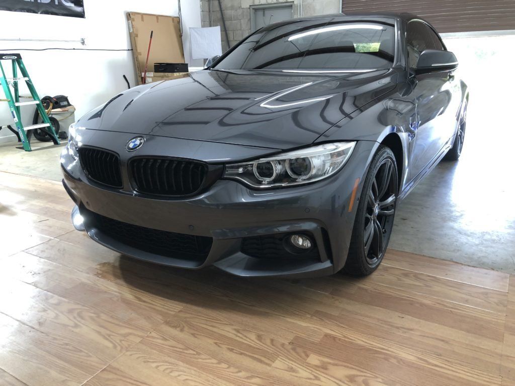 A gray bmw is parked on a wooden floor in a garage.