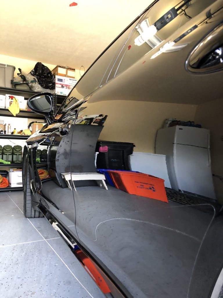 A car is parked in a garage filled with lots of items.