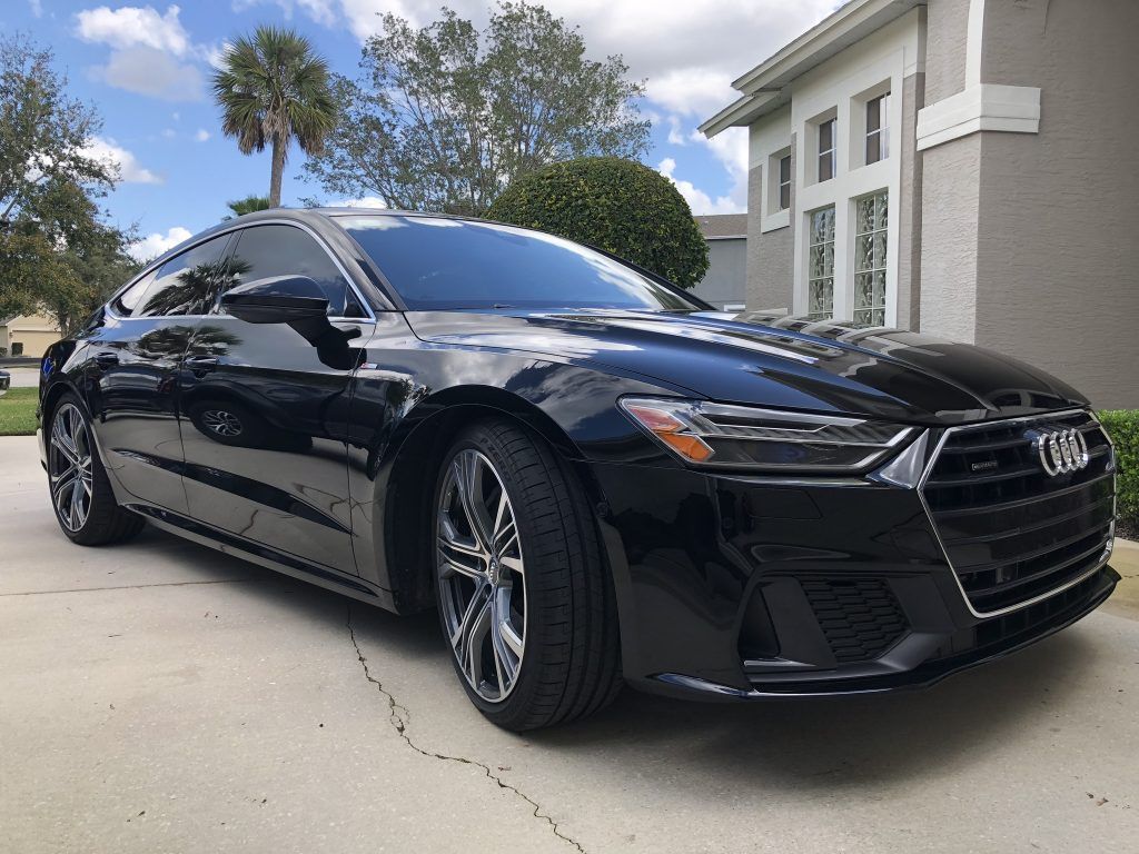 A black audi a7 is parked in a driveway in front of a house.