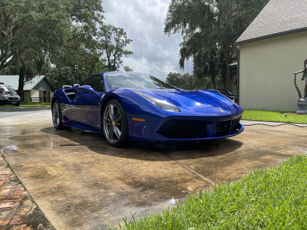 A blue ferrari 488 spider is parked in a driveway next to a house.