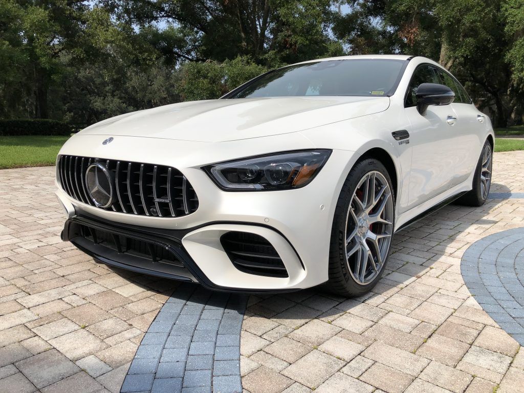 A white mercedes amg gt 63 s coupe is parked on a brick driveway.