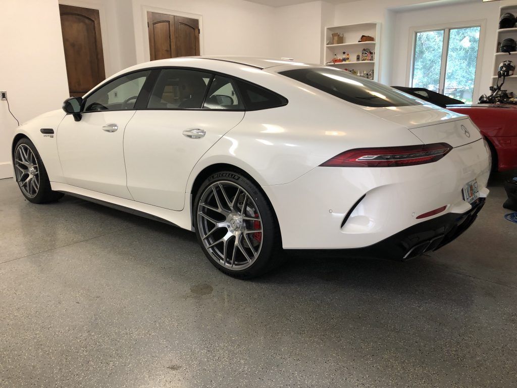 A white car is parked in a garage next to a red car.