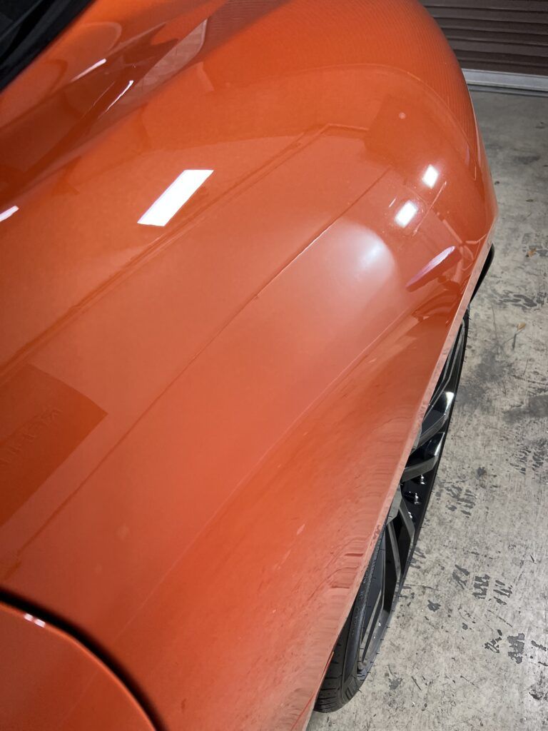 A close up of the side of an orange car in a garage.
