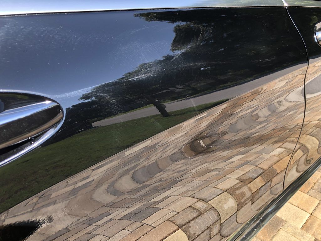 A black car is parked on a brick driveway.