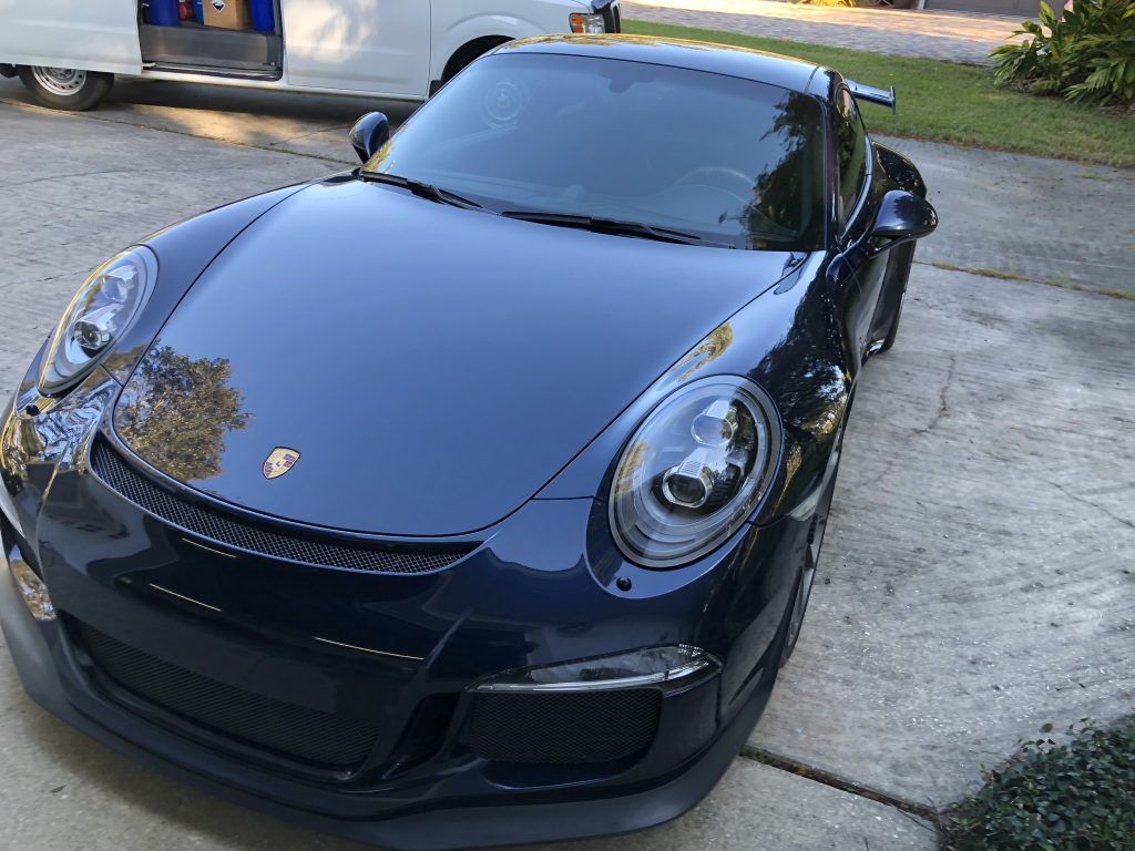 A black porsche 911 is parked in a driveway next to a white van.