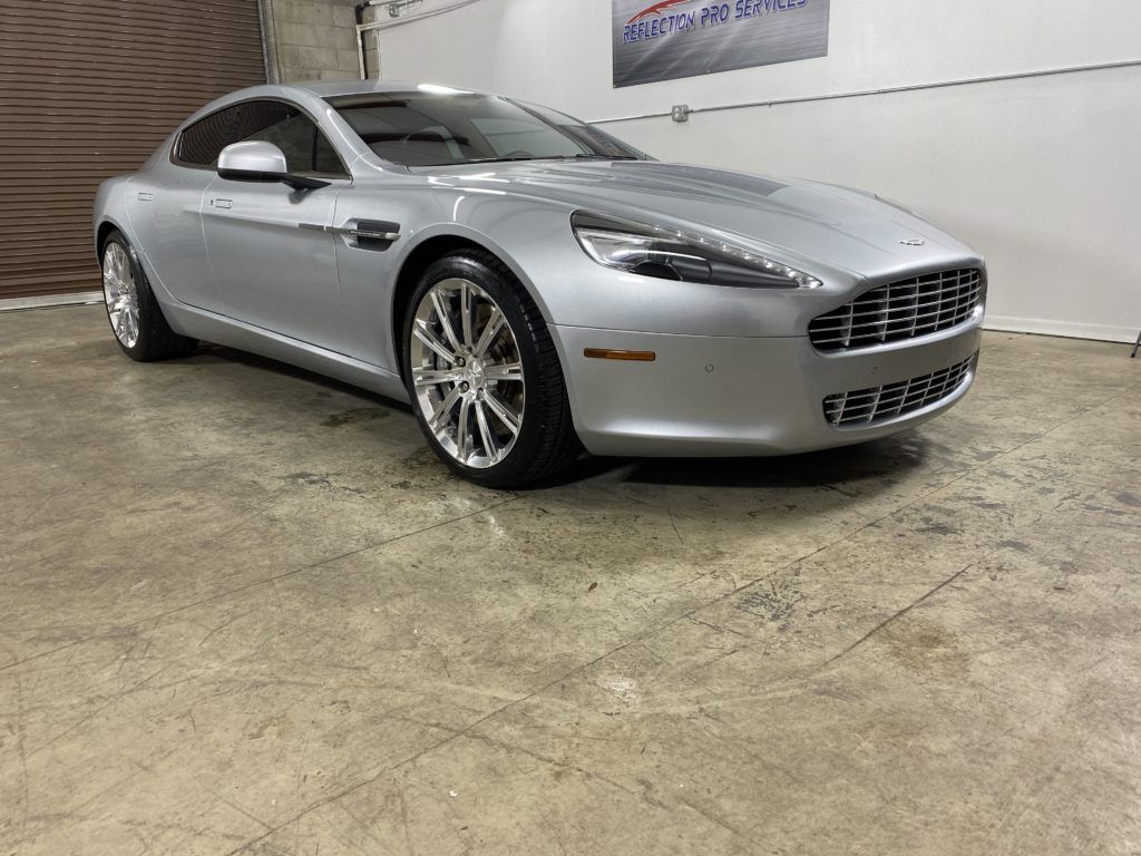 A silver aston martin rapide is parked in a garage.