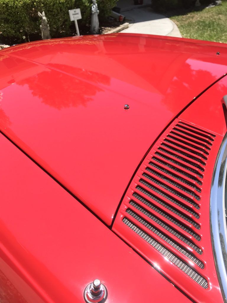 A close up of a red car 's hood and windshield