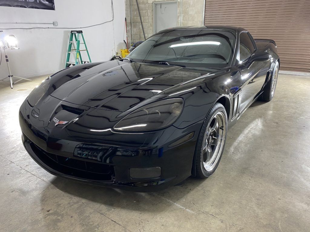 A black corvette is parked in a garage next to a ladder.