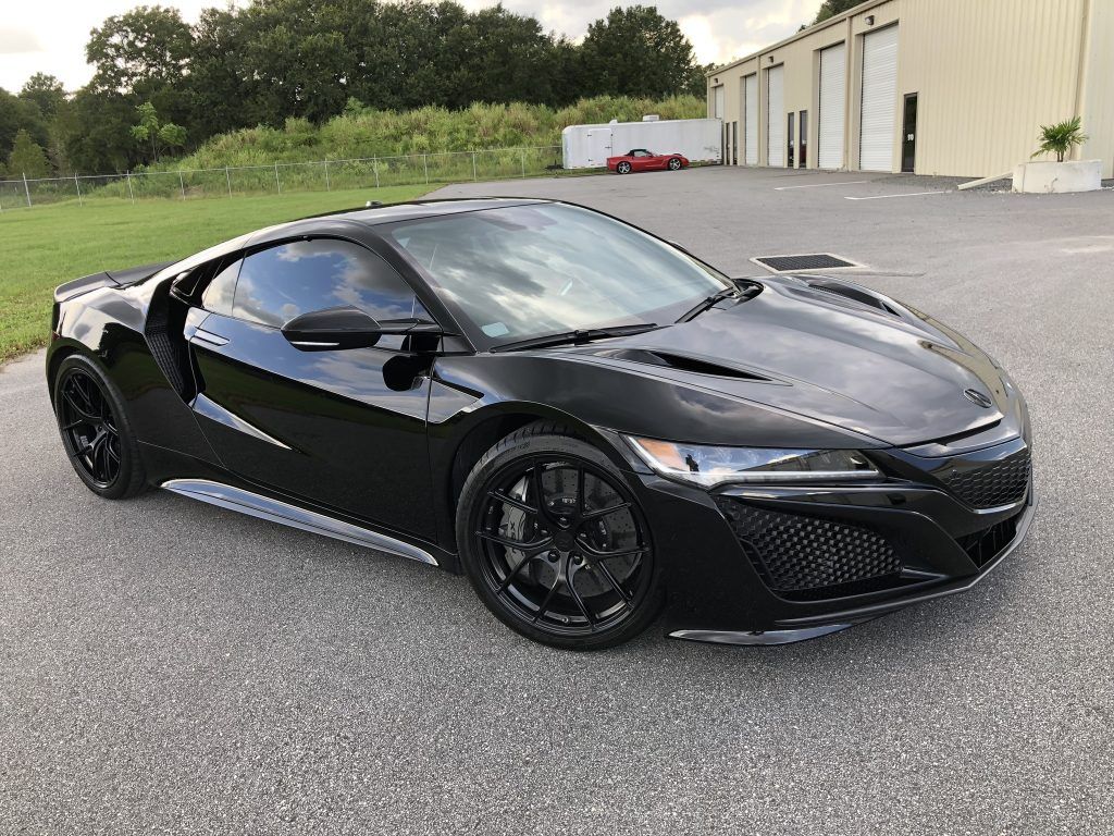 A black sports car is parked in a parking lot in front of a building.