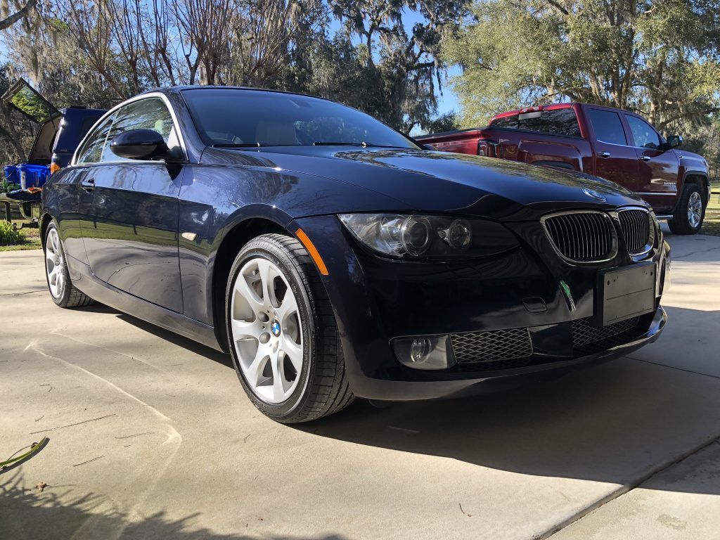 A black bmw is parked in a driveway next to a red truck.
