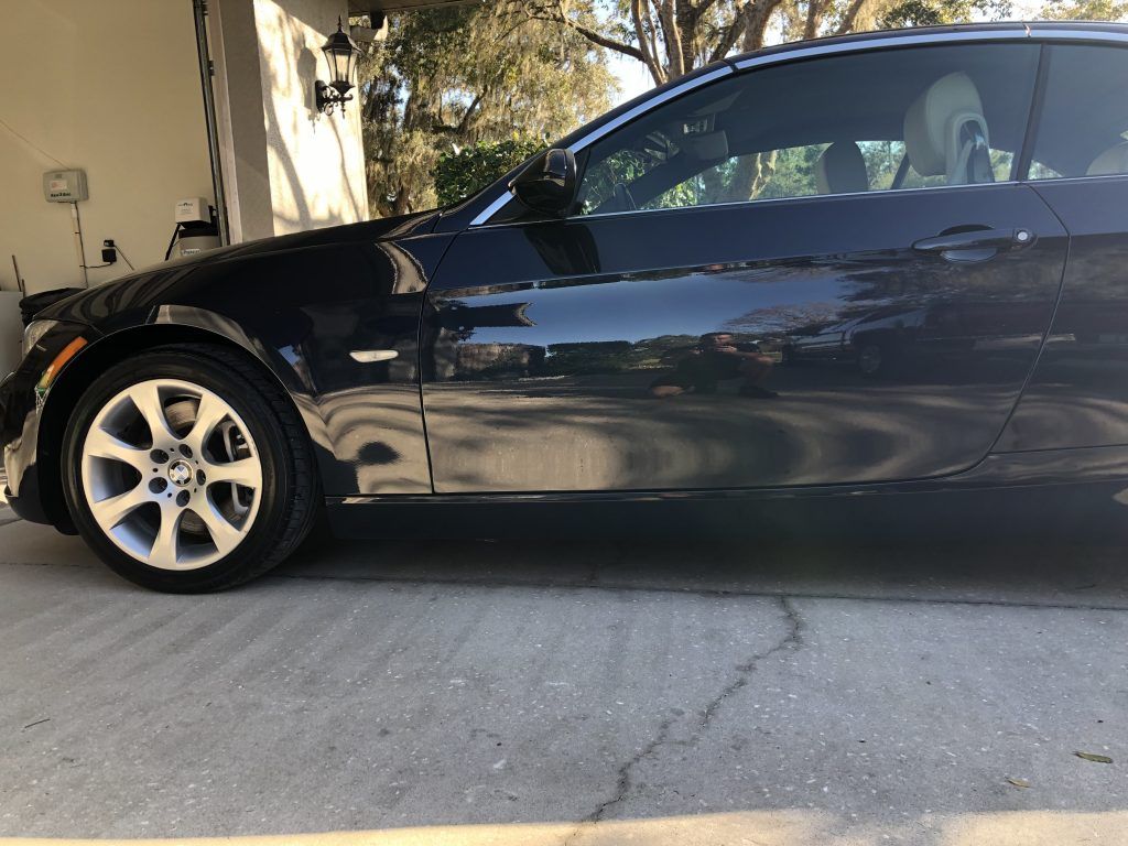 A black car is parked in a driveway next to a garage.
