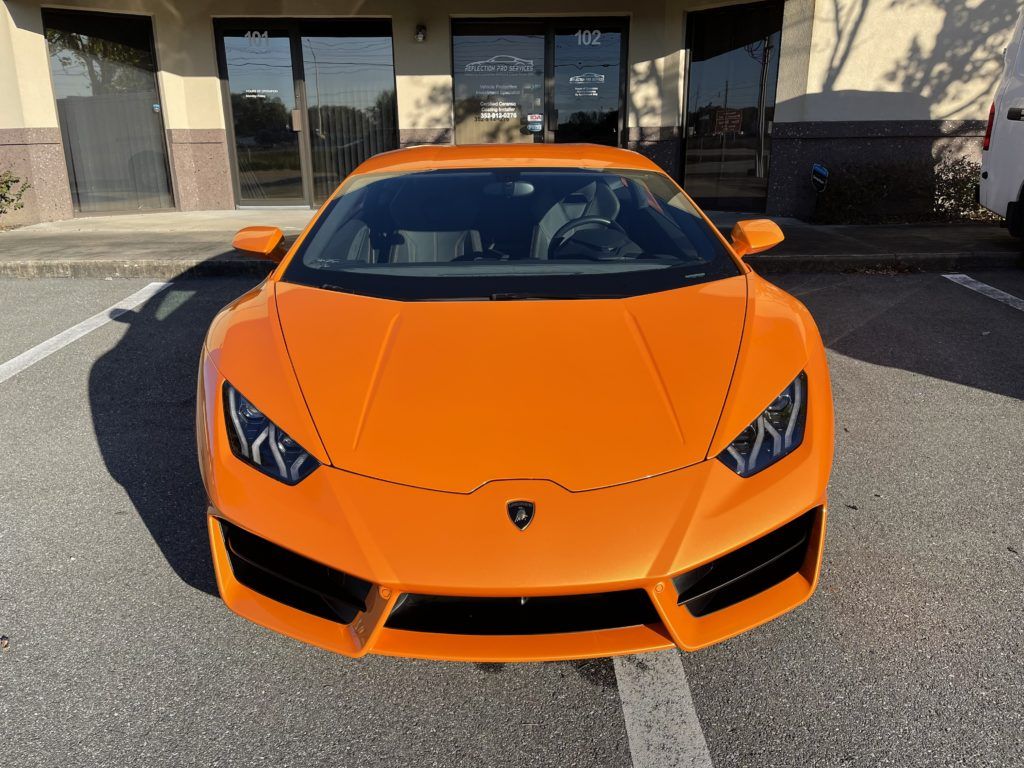 An orange lamborghini huracan is parked in a parking lot in front of a building.