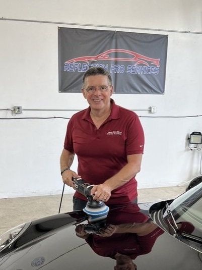 A man in a red shirt is polishing a black car.