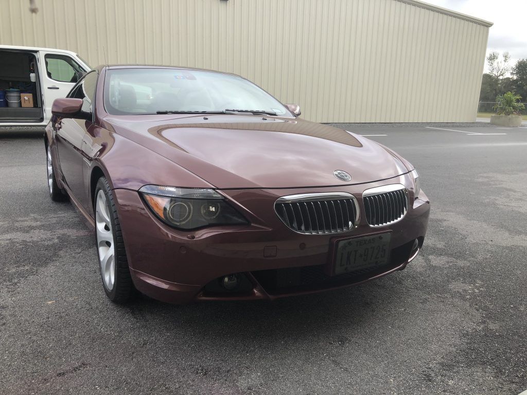 A brown bmw is parked in a parking lot in front of a building.