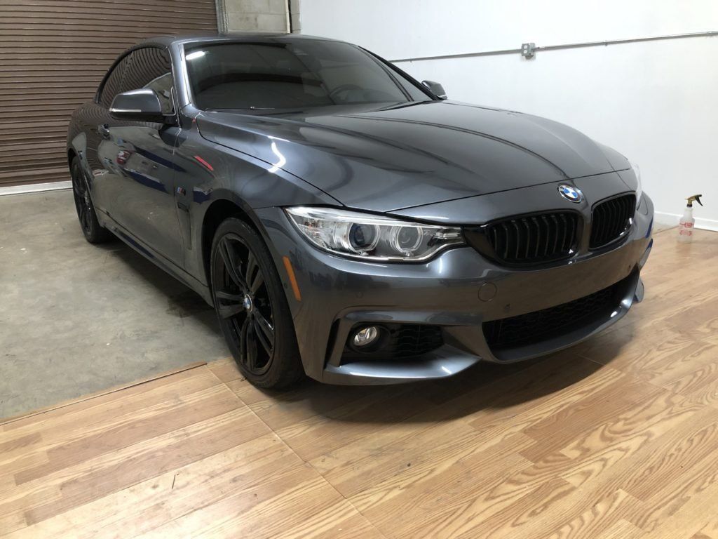 A gray bmw is parked in a garage on a wooden floor.