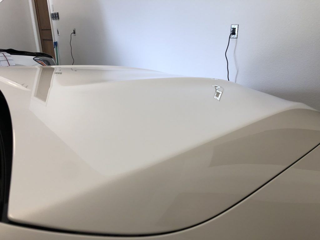 A white car is parked in a garage with the hood up.