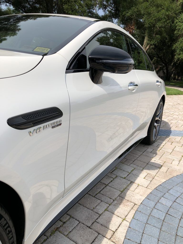 A white sports car is parked on a brick driveway.