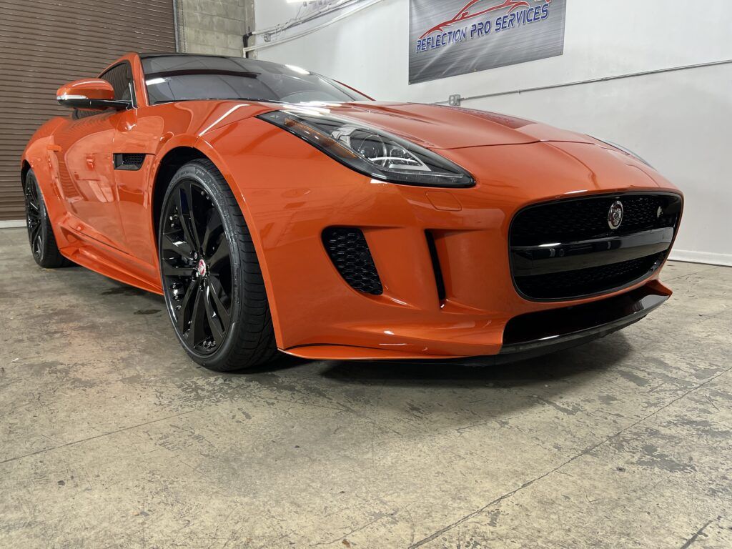An orange jaguar f type is parked in a garage.