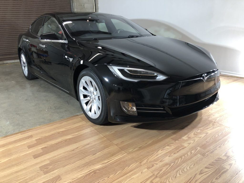 A black tesla model s is parked on a wooden floor in a garage.