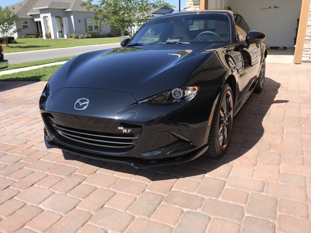 A black sports car is parked on a brick driveway.