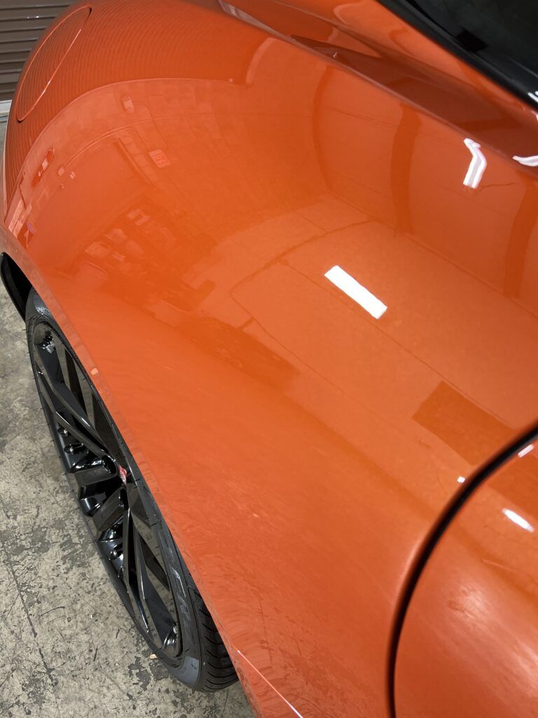 A close up of the side of an orange car with black wheels.