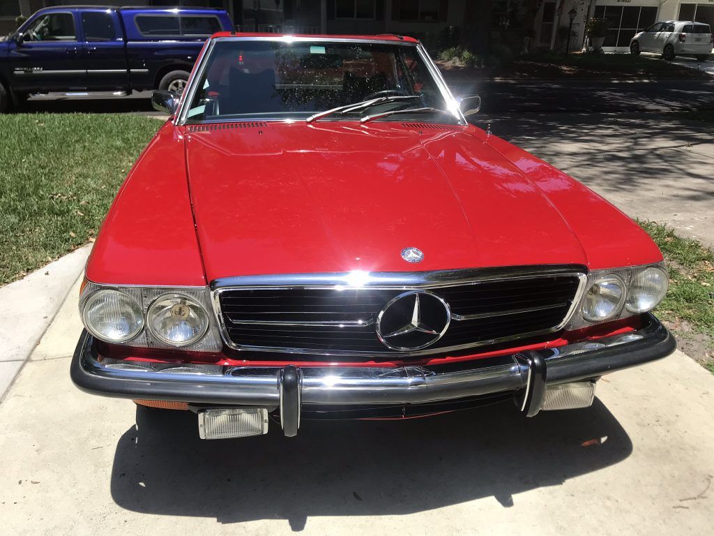 A red mercedes benz is parked on the side of the road.