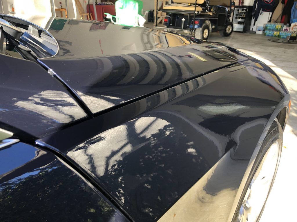 A black car is parked in a garage with a golf cart in the background.
