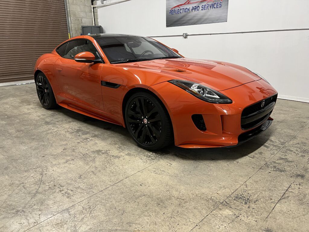 An orange jaguar f type is parked in a garage.