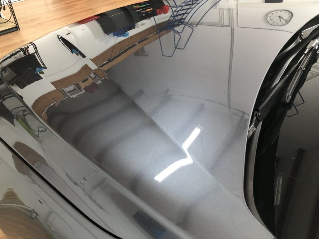 A close up of a car hood with a reflection of a clock in it