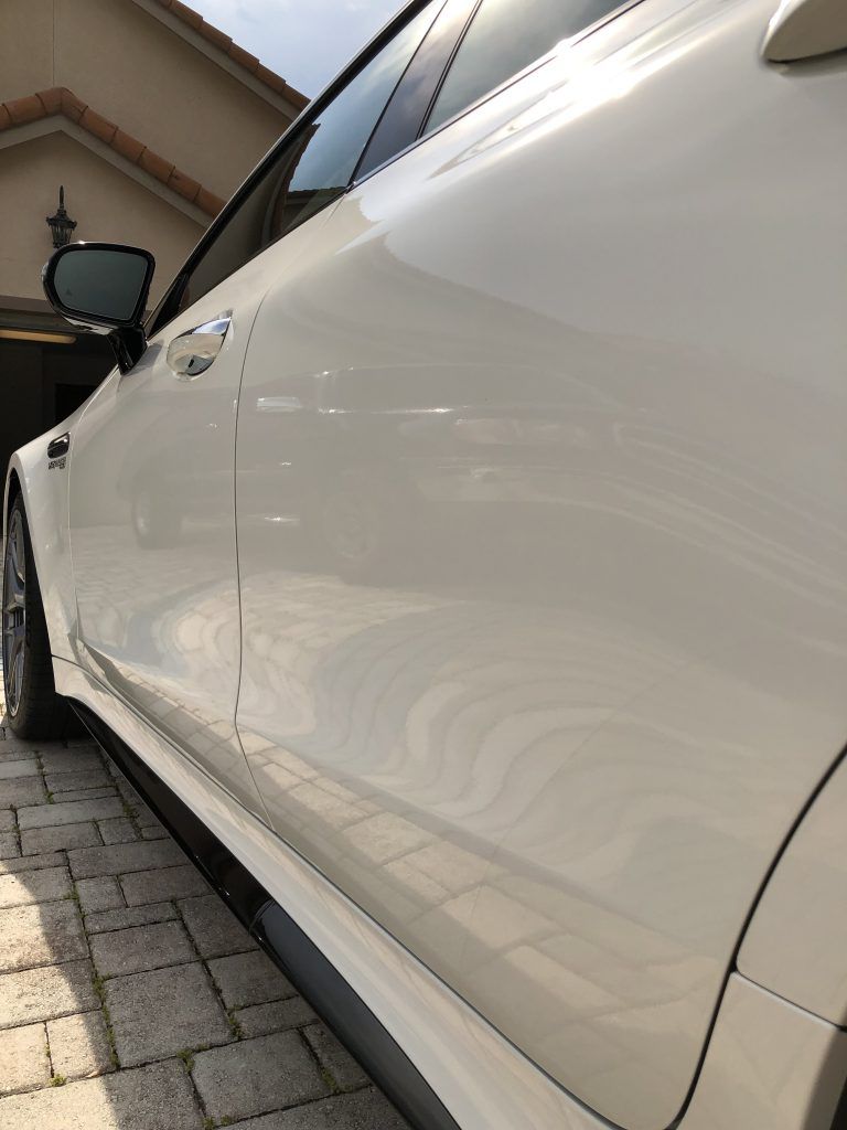 A white car is parked on a brick driveway in front of a house.