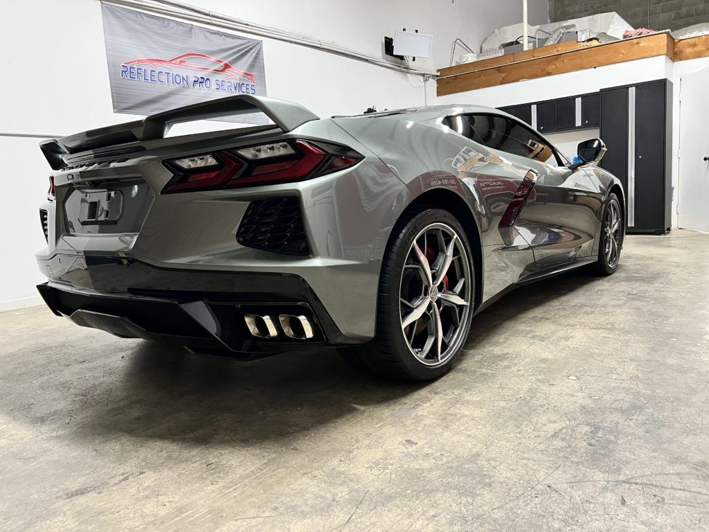 A gray sports car is parked in a garage next to a flag.