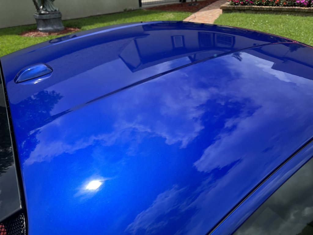 The roof of a blue car is reflecting the sky and clouds.