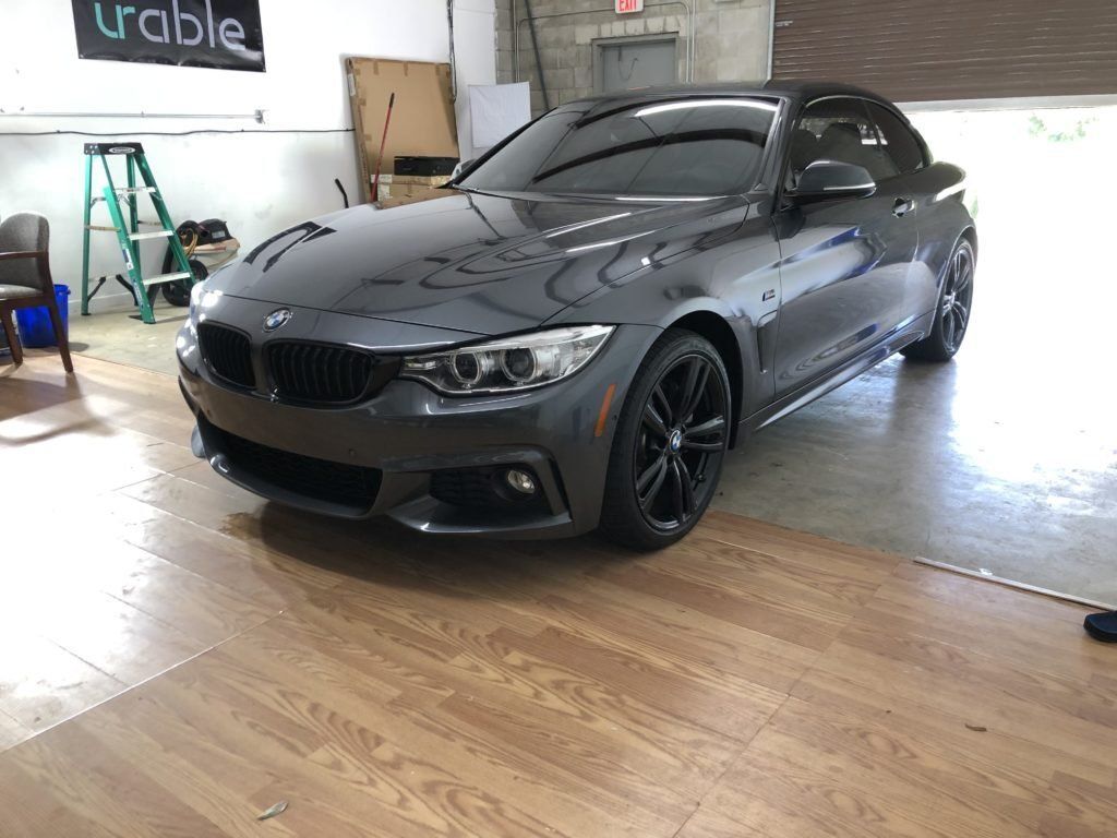 A gray bmw is parked in a garage on a wooden floor.