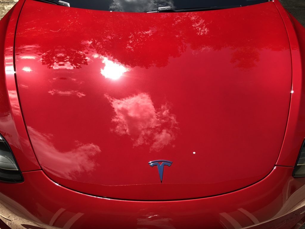 A red tesla model 3 with a blue t on the hood