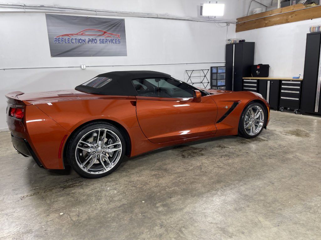 An orange corvette convertible is parked in a garage.