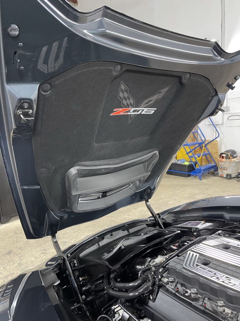 The hood of a black car is open in a garage.