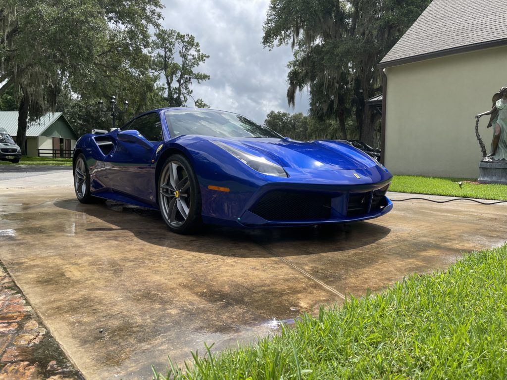 A blue ferrari 488 spider is parked in a driveway next to a house.