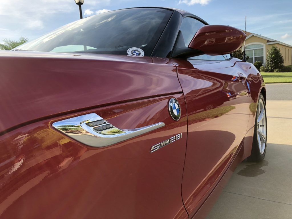A red bmw z4 is parked in a driveway next to a house.