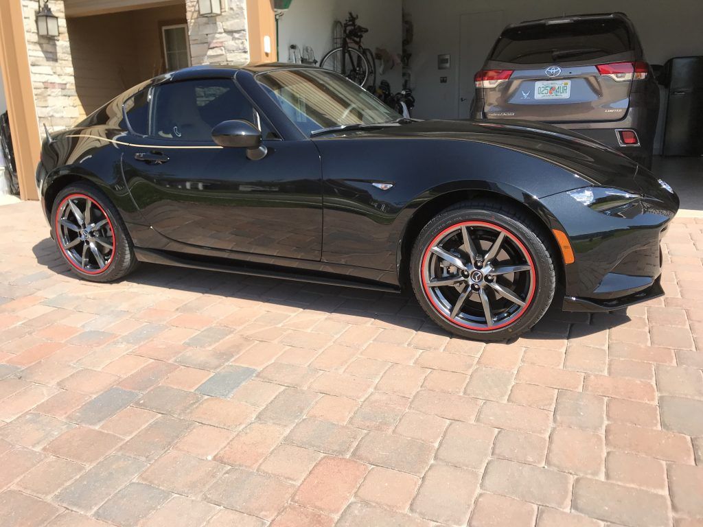 A black sports car with red wheels is parked on a brick driveway.