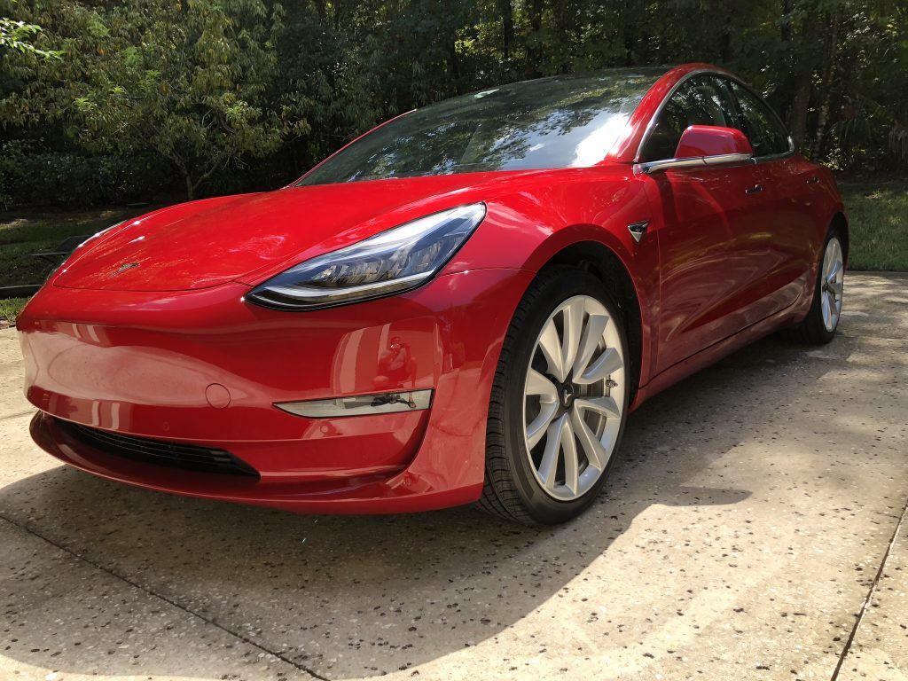 A red tesla model 3 is parked in a driveway.