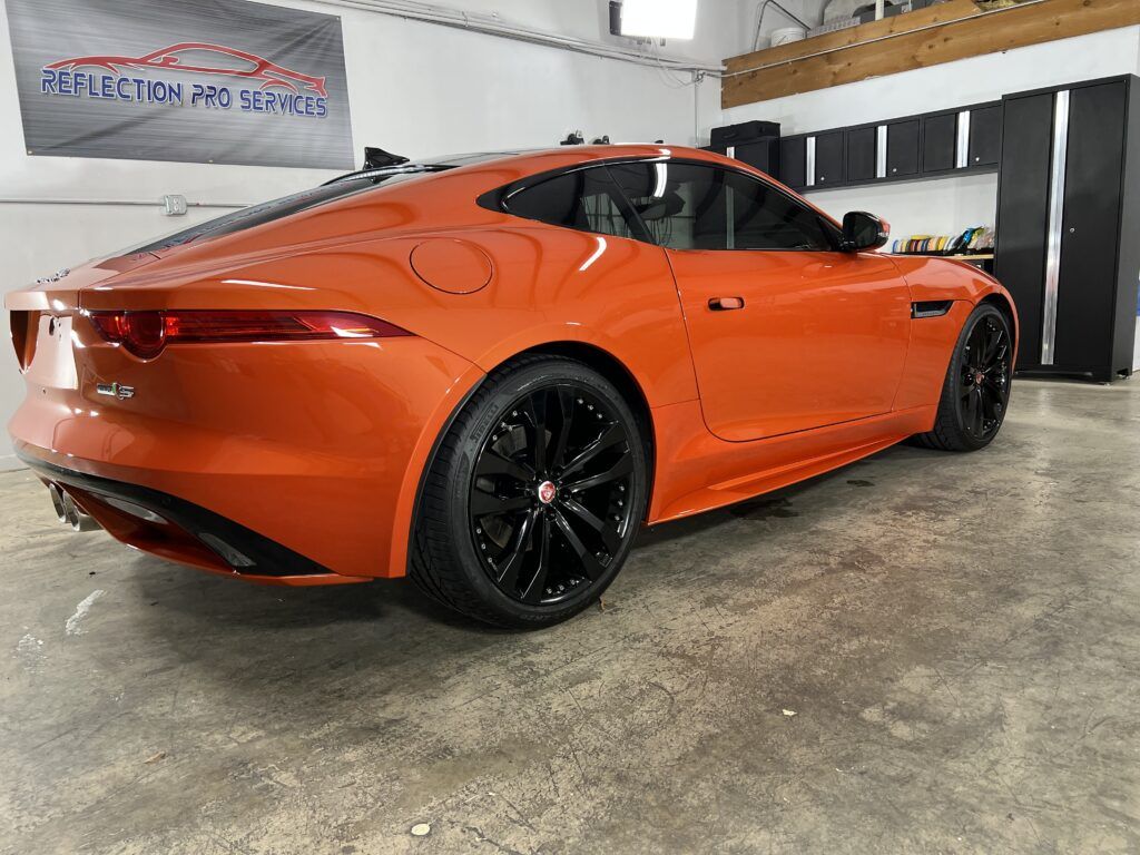 An orange jaguar f type is parked in a garage.