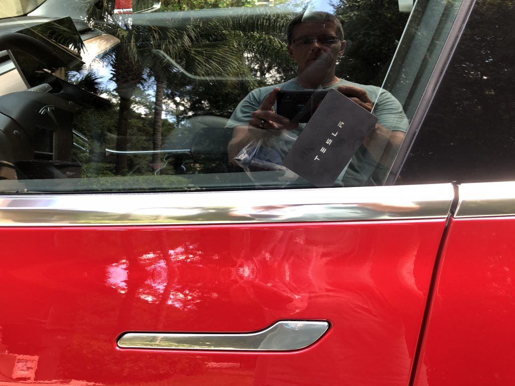 A man is taking a picture of himself in a red tesla car.