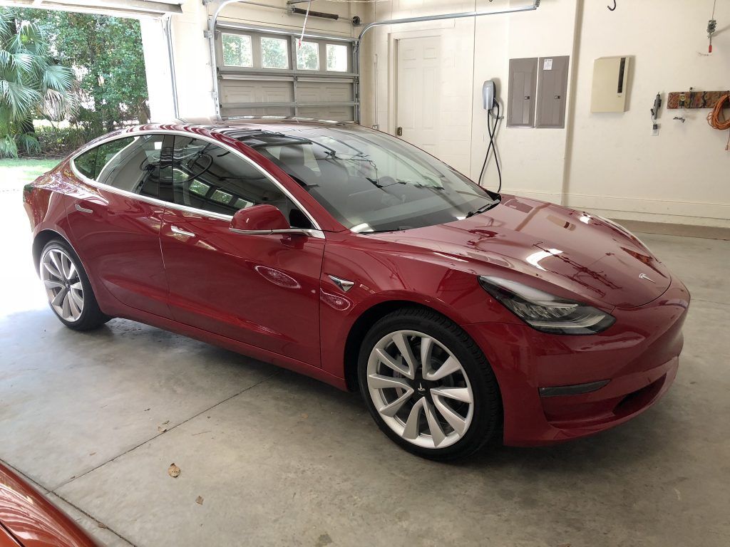 A red tesla model 3 is parked in a garage.