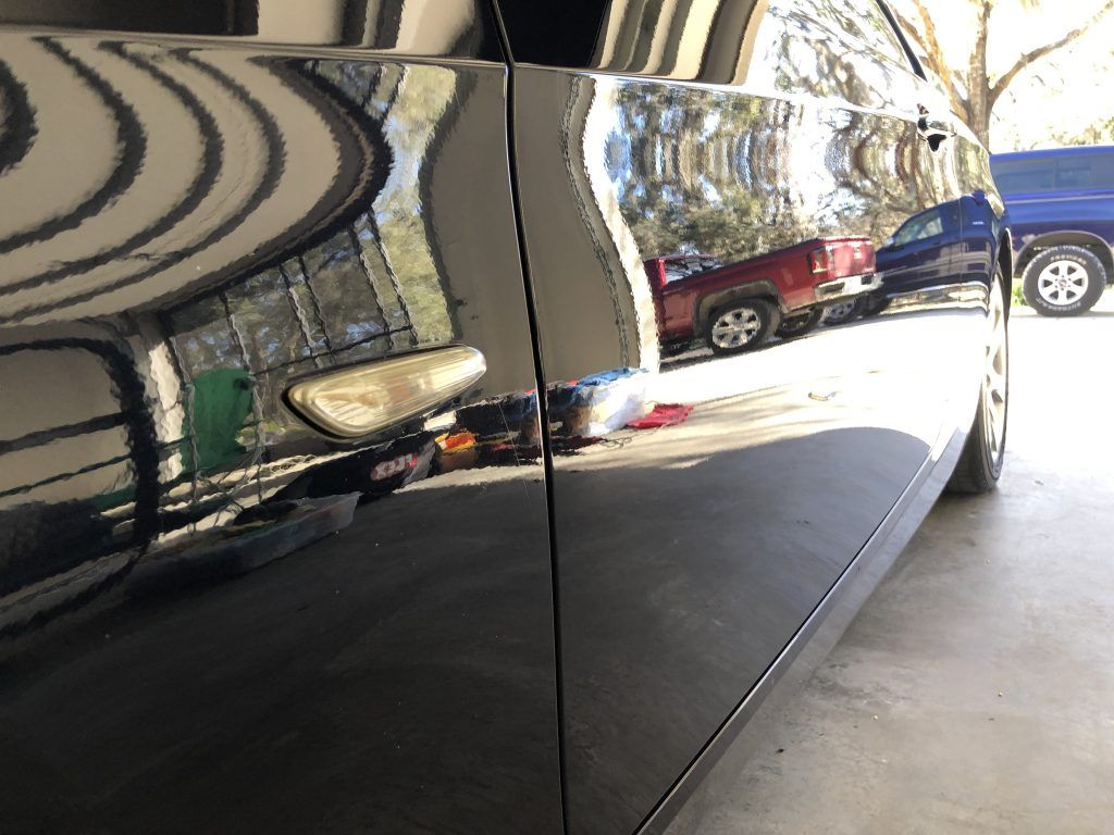 A black car is parked in a garage next to a red truck.