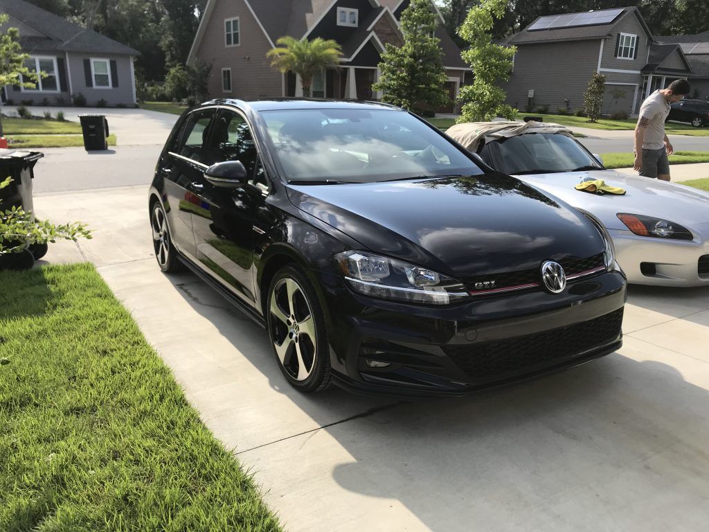 A black car is parked in a driveway next to a white car.