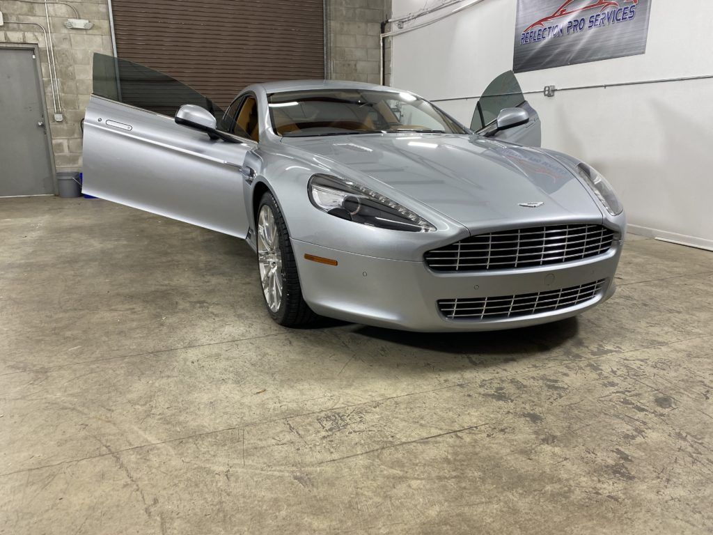 A silver sports car is parked in a garage with its doors open.